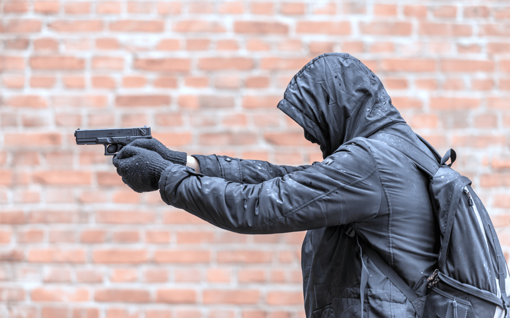A man in a hooded jacket in profile, holding a gun. The image represents the rise in gun-related deaths.